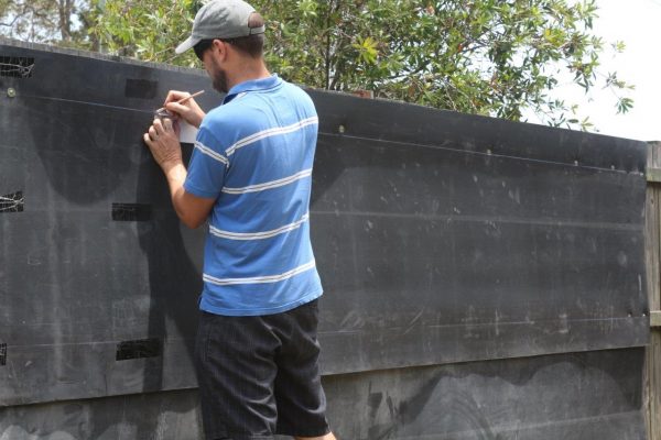A man in a blue t-shirt drawing markings on his fence for acoustic fence wrapping
