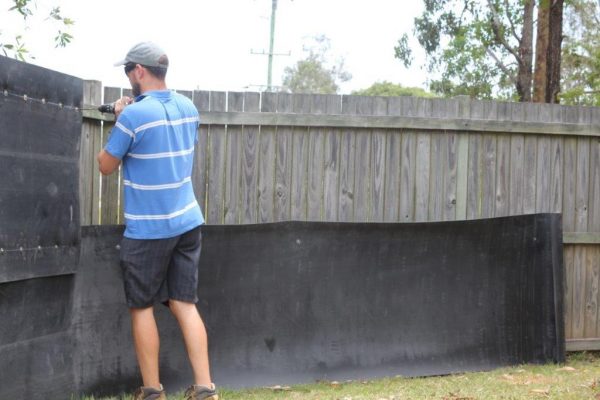 Man drilling his resilient acoustic fence wrap securely in his backyard